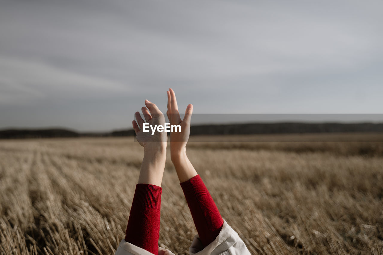 Cropped hand of woman on field against sky