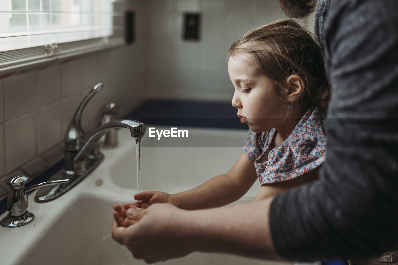 Side view of young girl having hands washed by dad