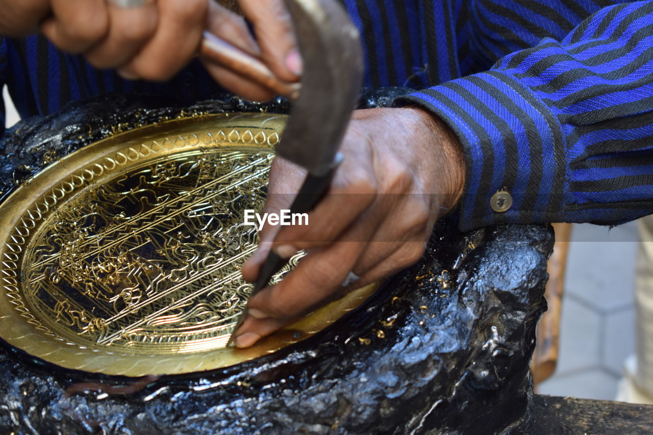 Midsection of man carving metal on rock