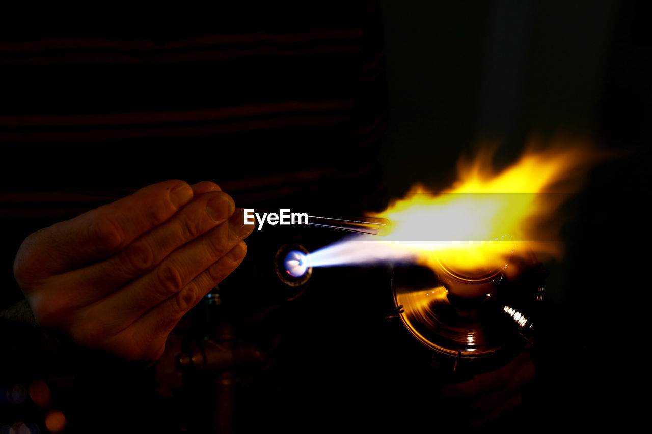 Close-up of hand heating metal in darkroom