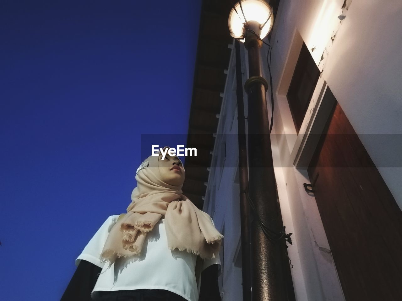 Low angle view of woman standing by illuminated street light against building at night