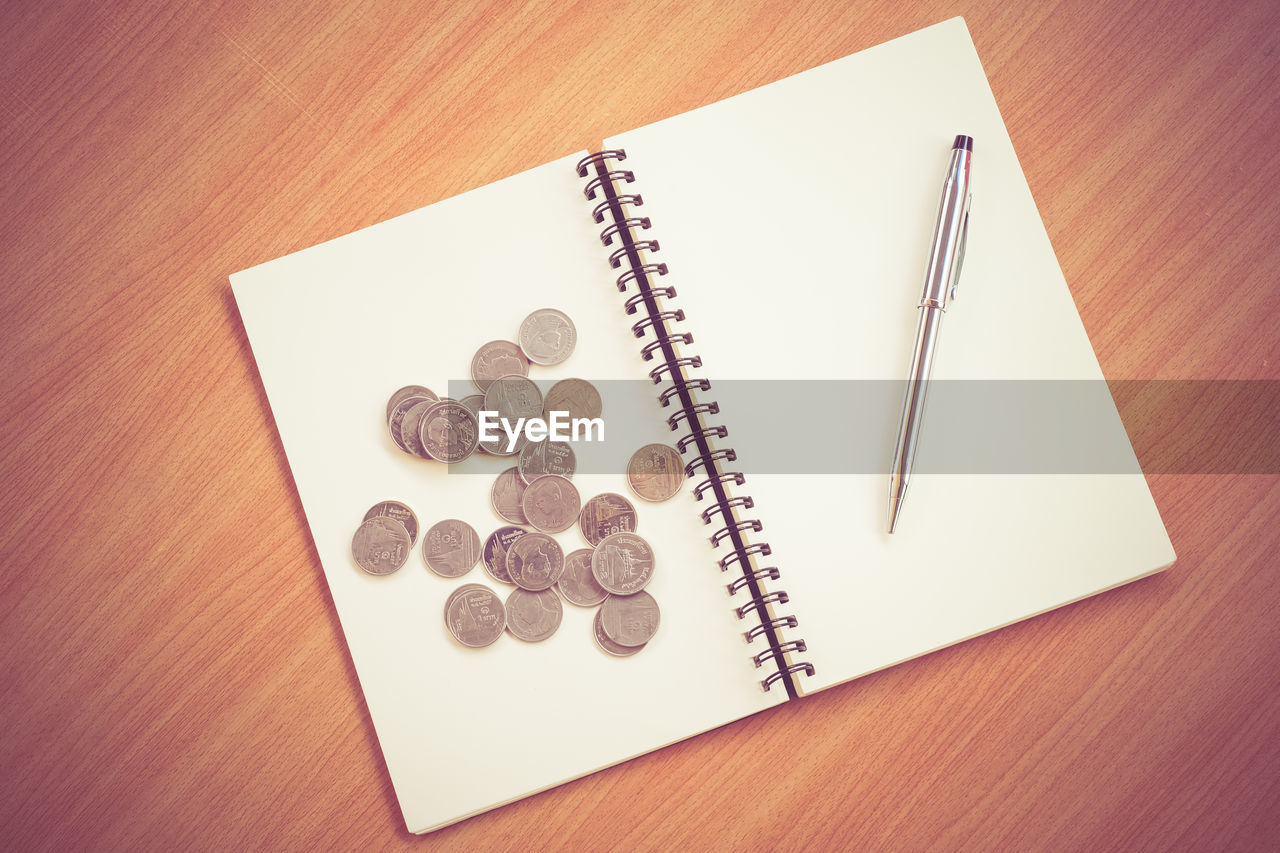 Directly above shot of open book with pen and coins on wooden table