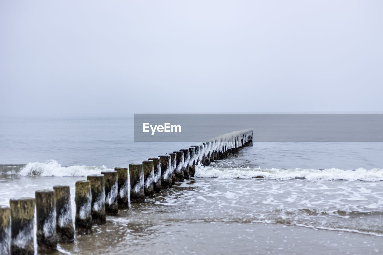 WOODEN POSTS ON BEACH AGAINST CLEAR SKY