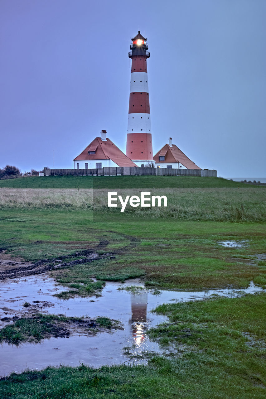 Lighthouse on field by building against sky