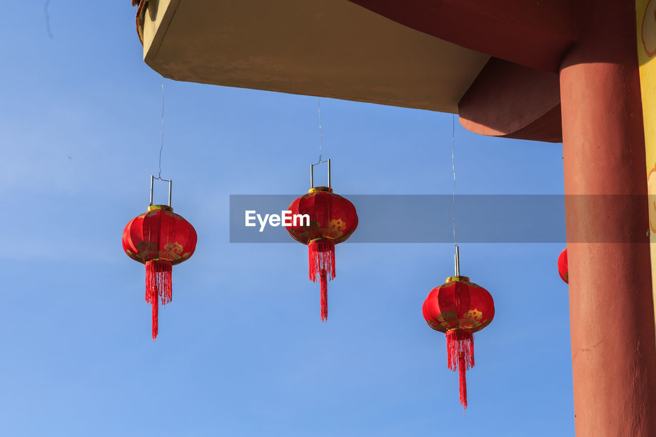 Low angle view of lanterns hanging on building against blue sky