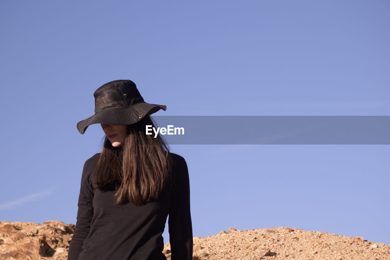 Woman wearing hat standing against clear blue sky