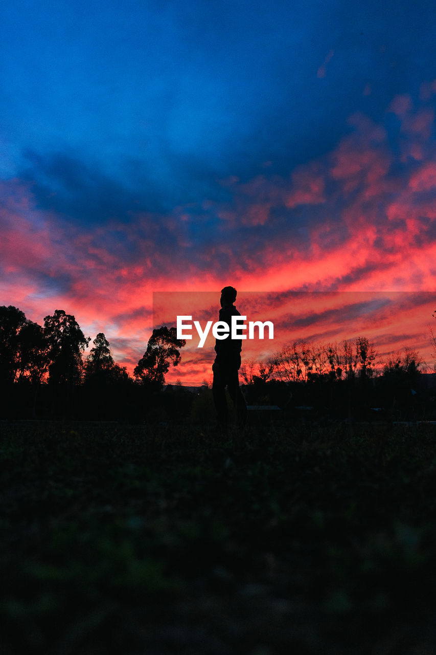 SILHOUETTE MAN STANDING ON FIELD AGAINST SKY AT SUNSET