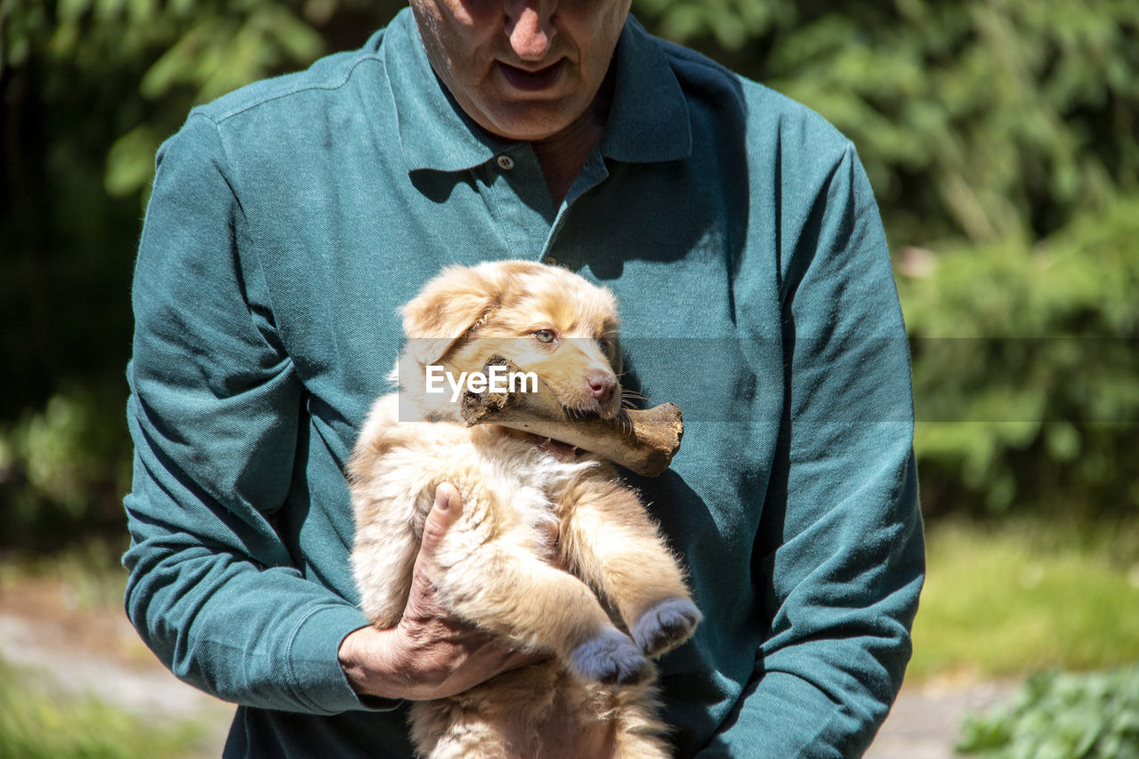 Man holding small dog with bone in his mouth