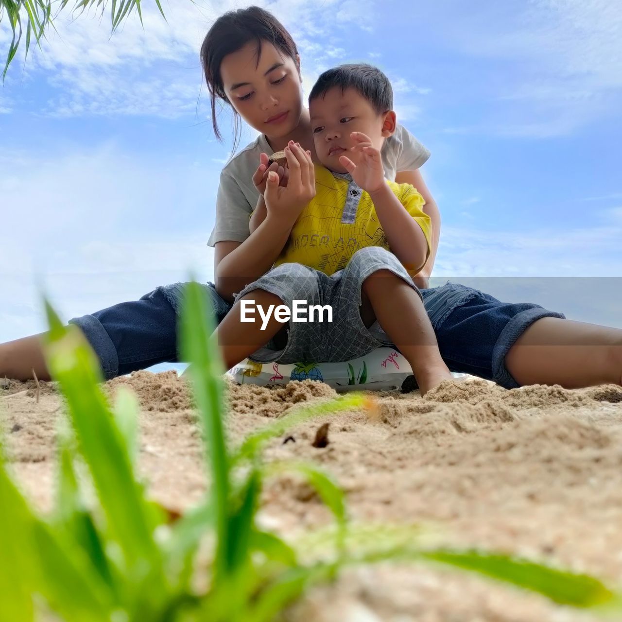 Mother and son sitting on sand against sky