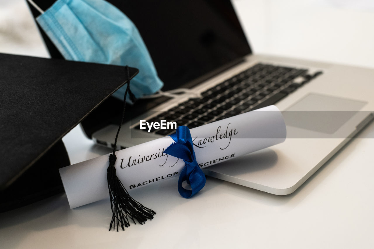 Closeup of graduation hat with degree and surgical mask on white background. virtual celebration