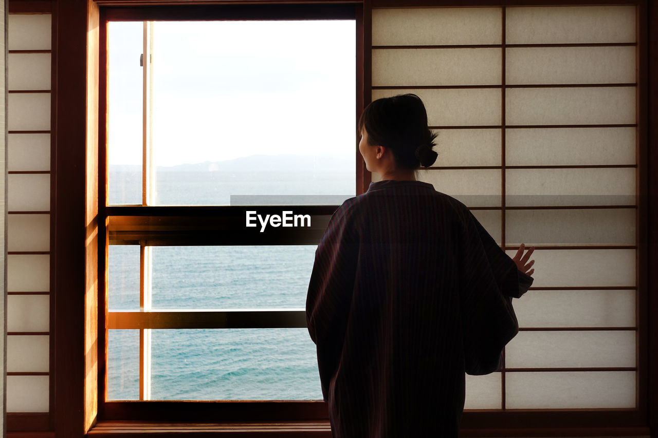 Rear view of woman looking at sea through window