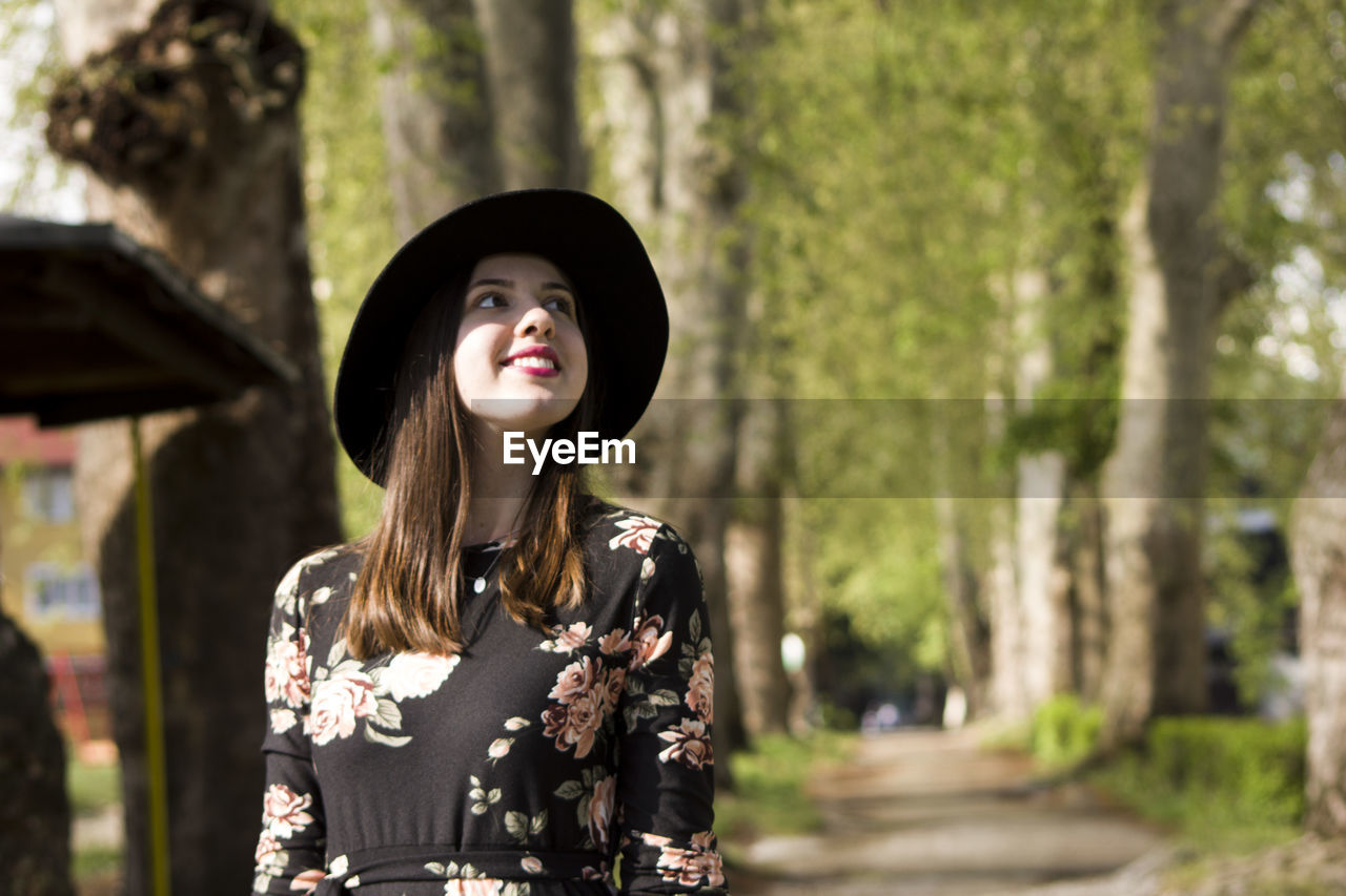 Young woman wearing hat standing against trees