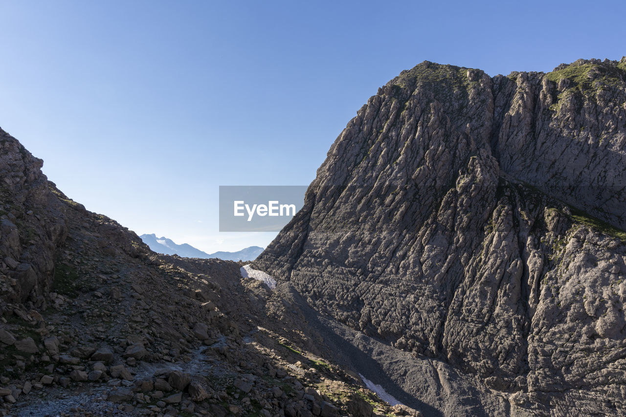 mountain, environment, landscape, sky, scenics - nature, beauty in nature, nature, wilderness, rock, ridge, land, adventure, clear sky, mountain range, travel destinations, travel, blue, geology, no people, non-urban scene, outdoors, walking, sunny, activity, summit, mountain pass, day, tranquility, tree, plant, tourism, rock formation, plateau, outdoor pursuit, leisure activity, mountain peak, tranquil scene, terrain, pinaceae, coniferous tree, cliff, sunlight, cloud, pine tree