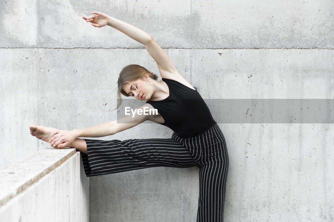Dancer in black striped pants stretching in front of concrete wall