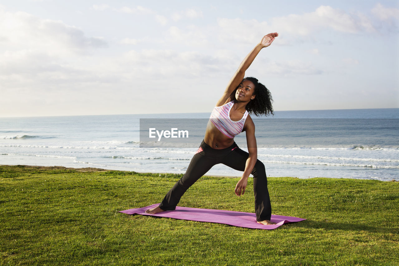 Woman exercising on field against sky