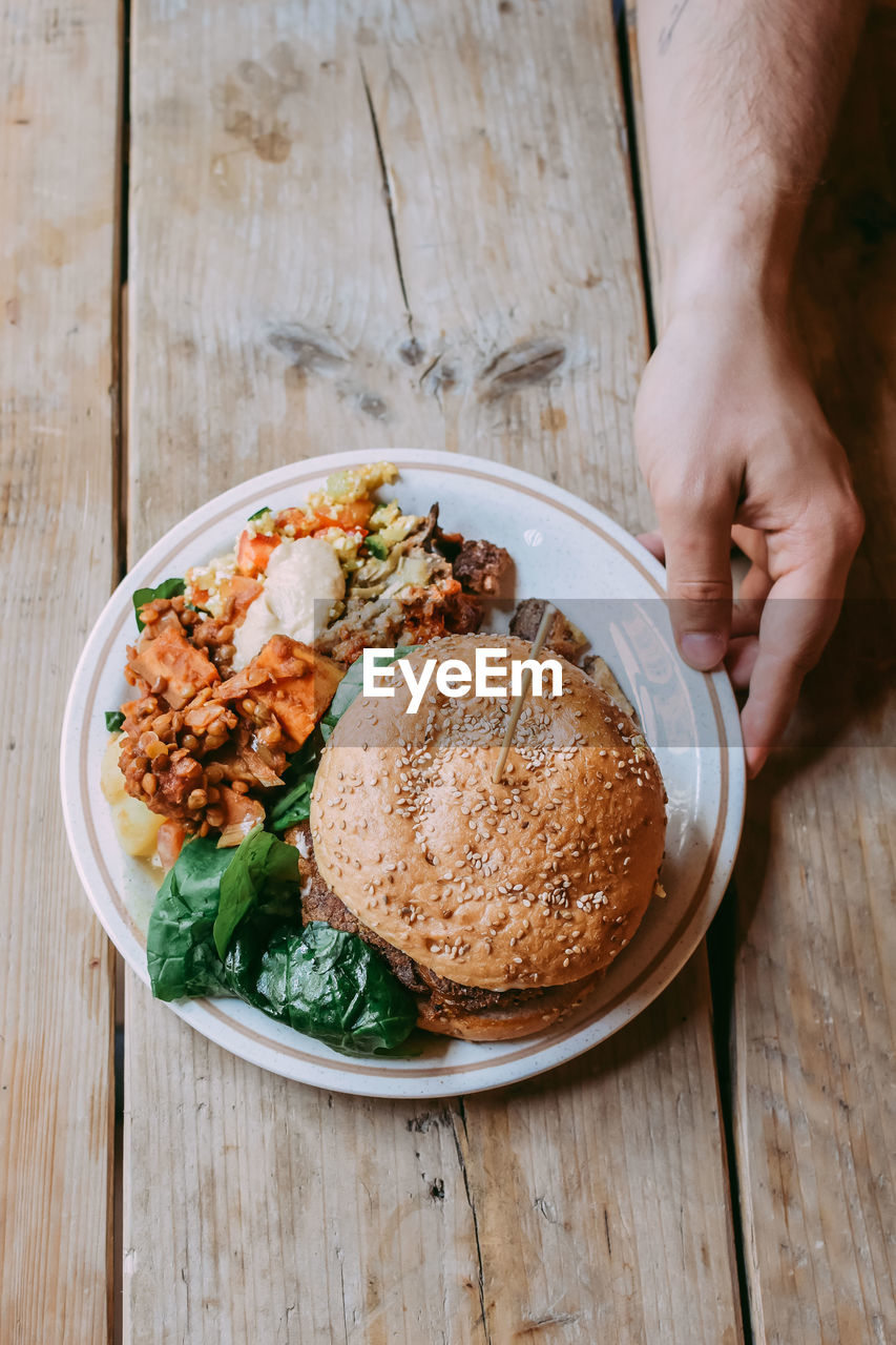 Cropped hand holding food in plate on wooden table