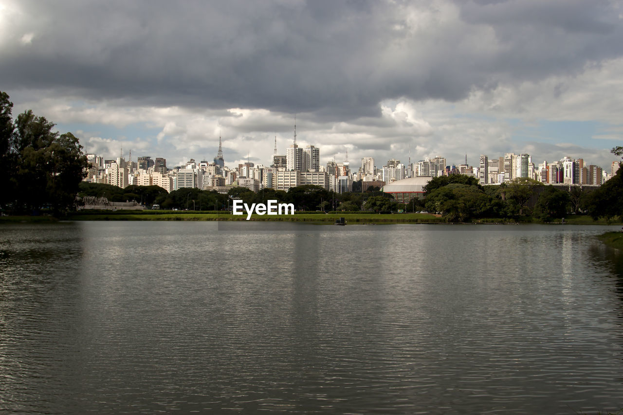 View of city at waterfront against cloudy sky