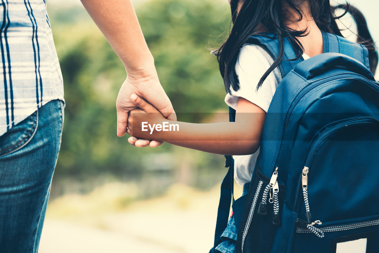 Midsection of mother holding daughter hand while taking her to school