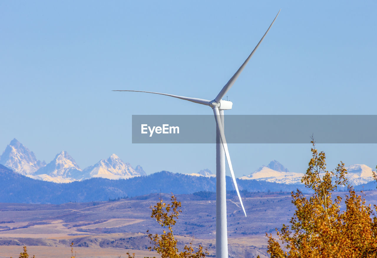Wind turbines in field against blue sky and mountains