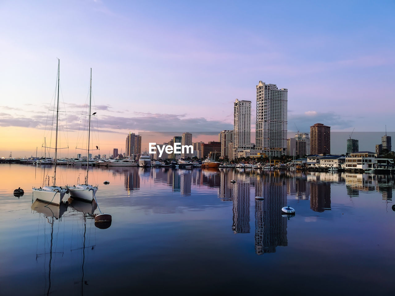 SAILBOATS MOORED IN SEA AGAINST BUILDINGS IN CITY