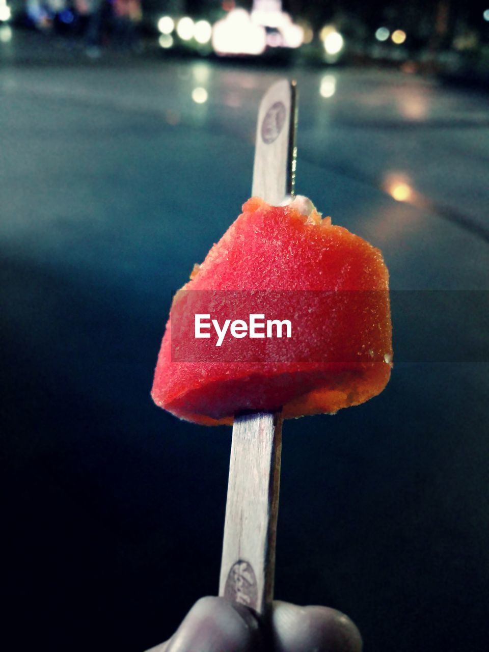 Cropped image of hand holding ice candy over city