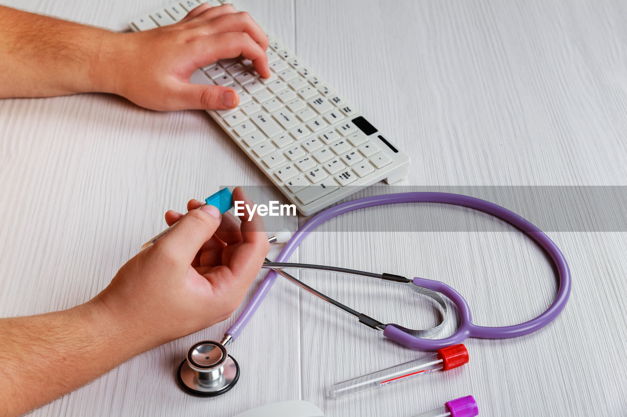 Cropped hand of person holding medical equipment by stethoscope and computer on desk