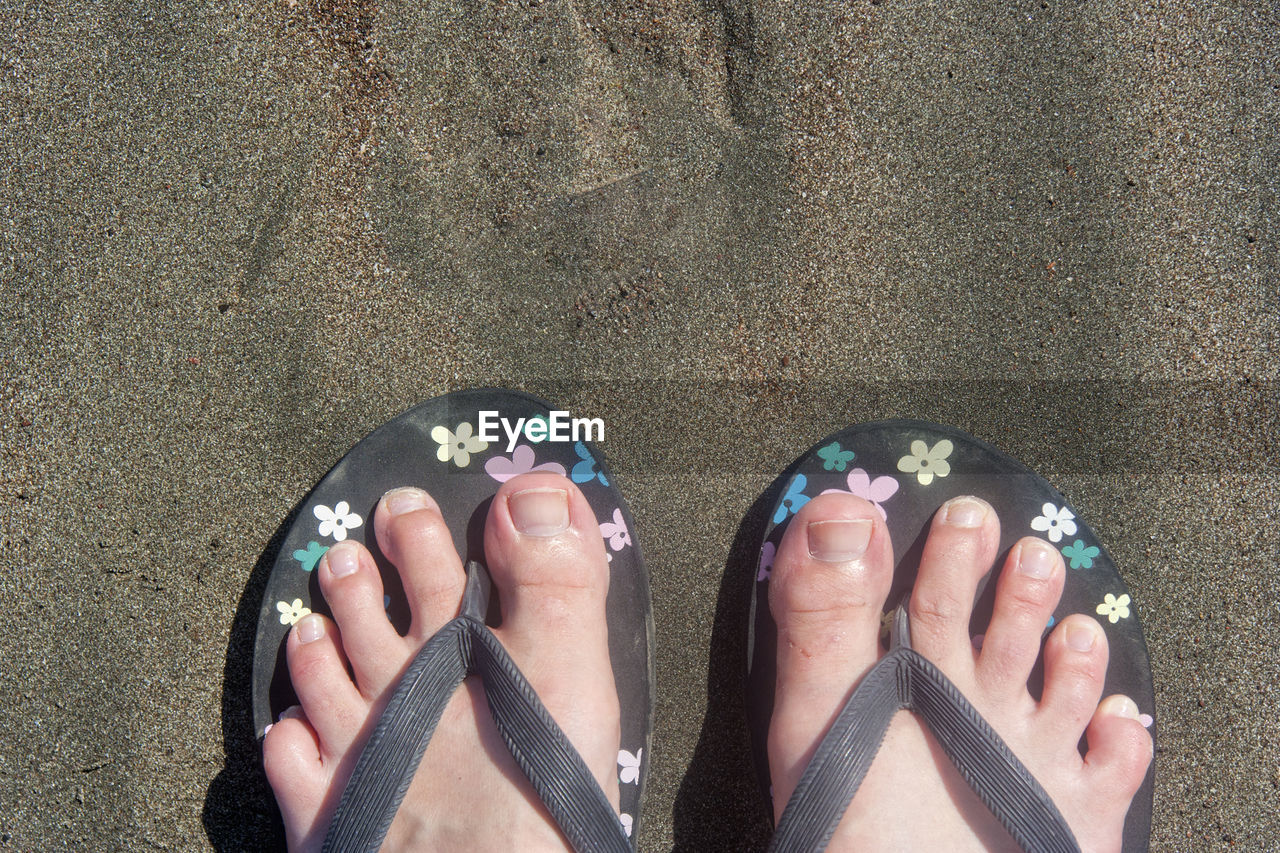 Low section of person wearing flip-flop at beach