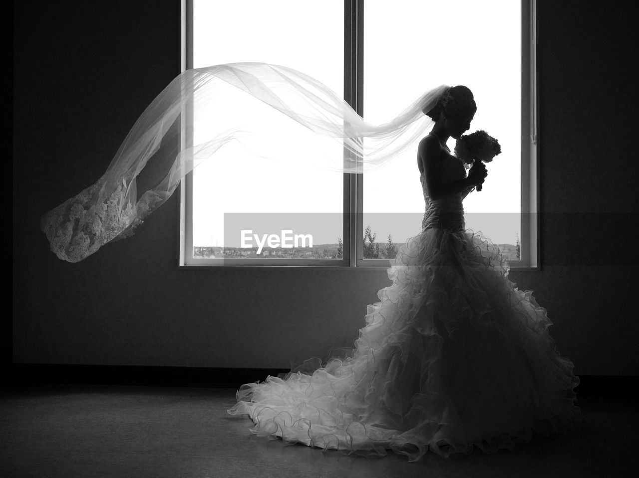 Bride in dress standing by window at home