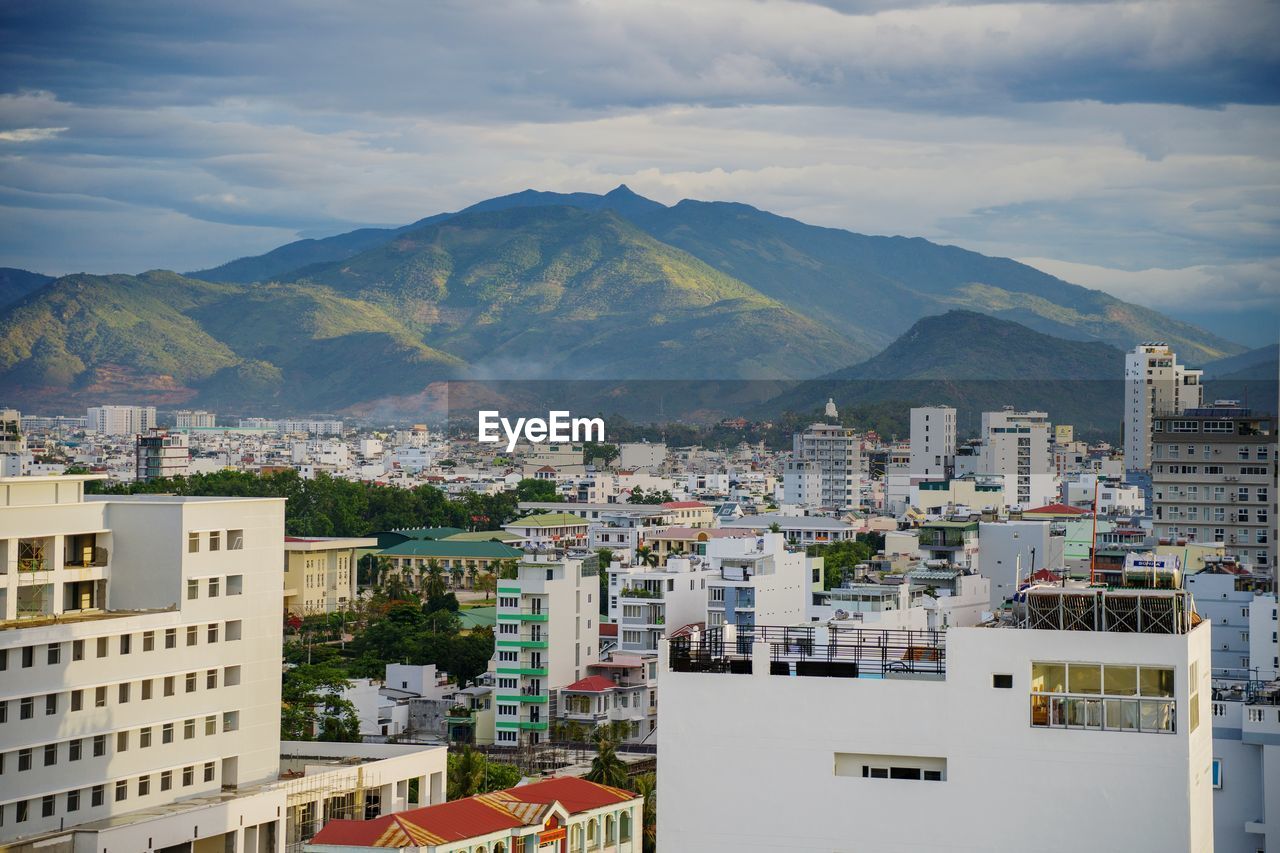 High angle view of townscape by mountain against cloudy sky