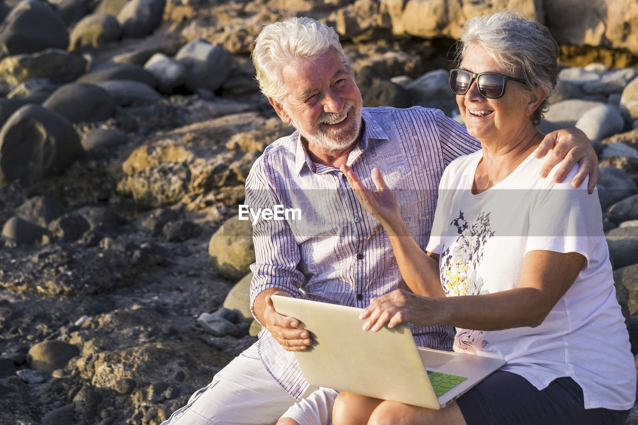 Cheerful couple using laptop while sitting at beach