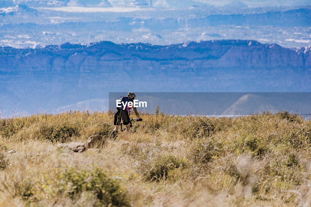 Rear view of man with bicycle on mountain against sky