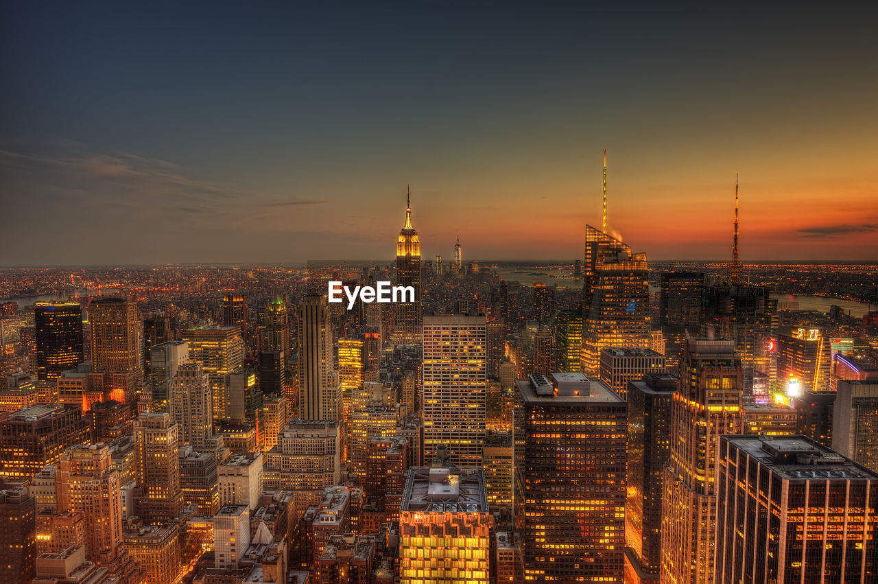 Illuminated buildings in city against sky during sunset