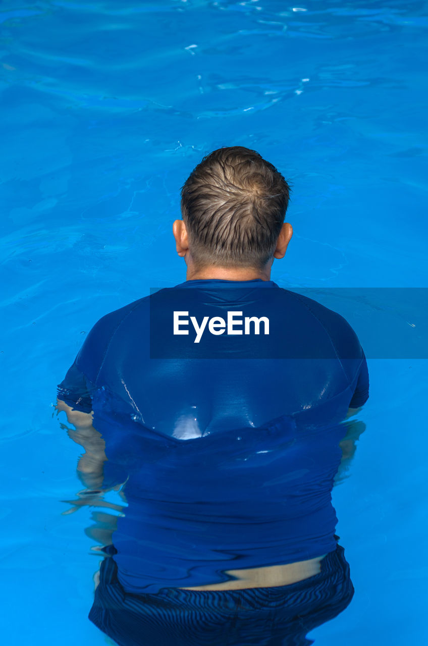 REAR VIEW OF SHIRTLESS MAN SWIMMING IN POOL