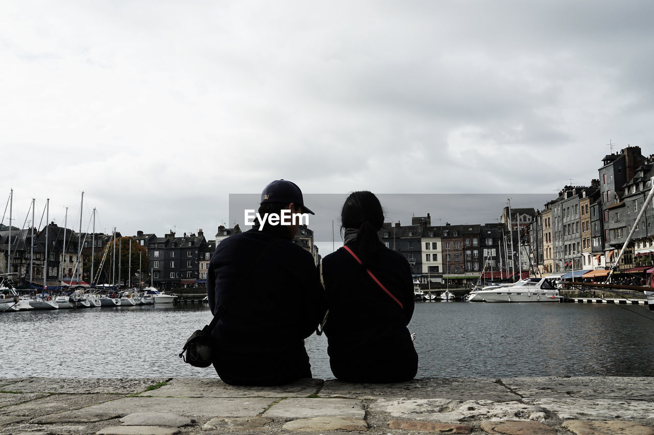 Rear view of couple sitting on pier at harbor