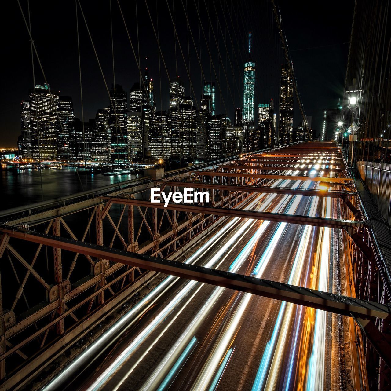 Light trails on bridge over river by buildings at night