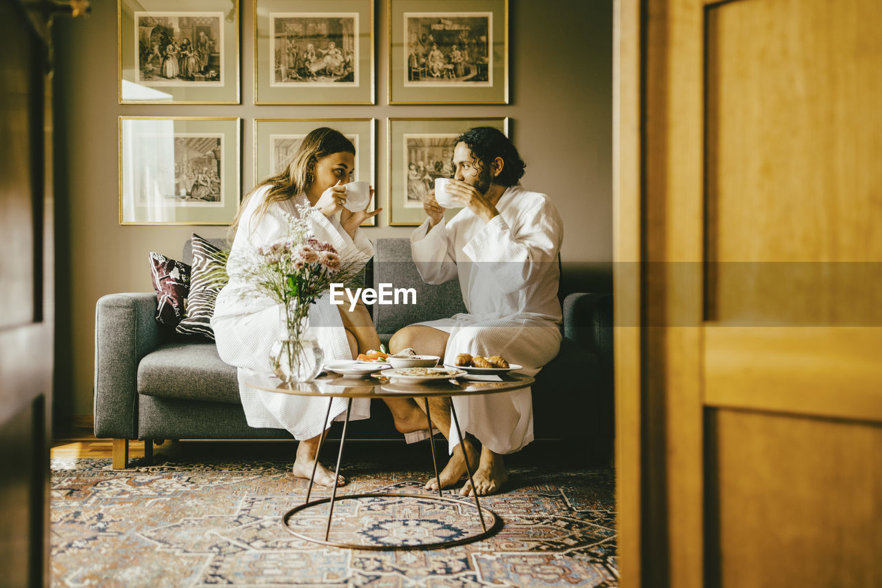 Couple in bathrobes drinking coffee while enjoying breakfast at hotel