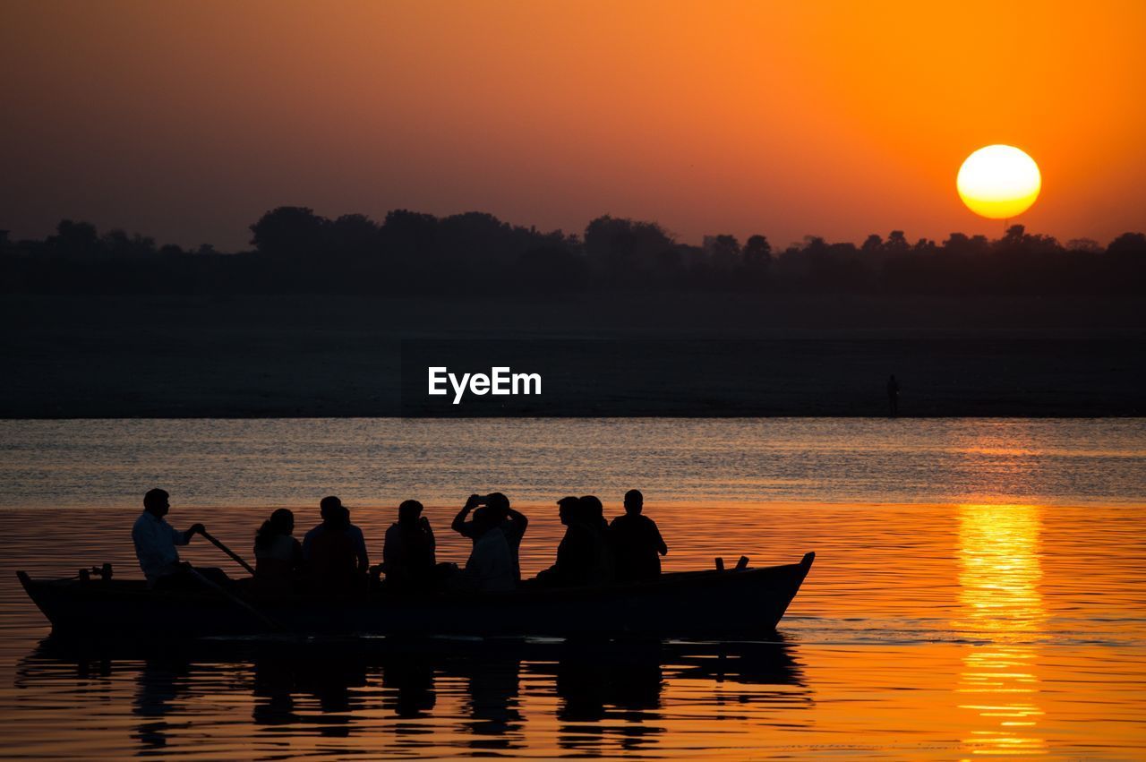 Silhouette people in boat on lake against sky during sunset