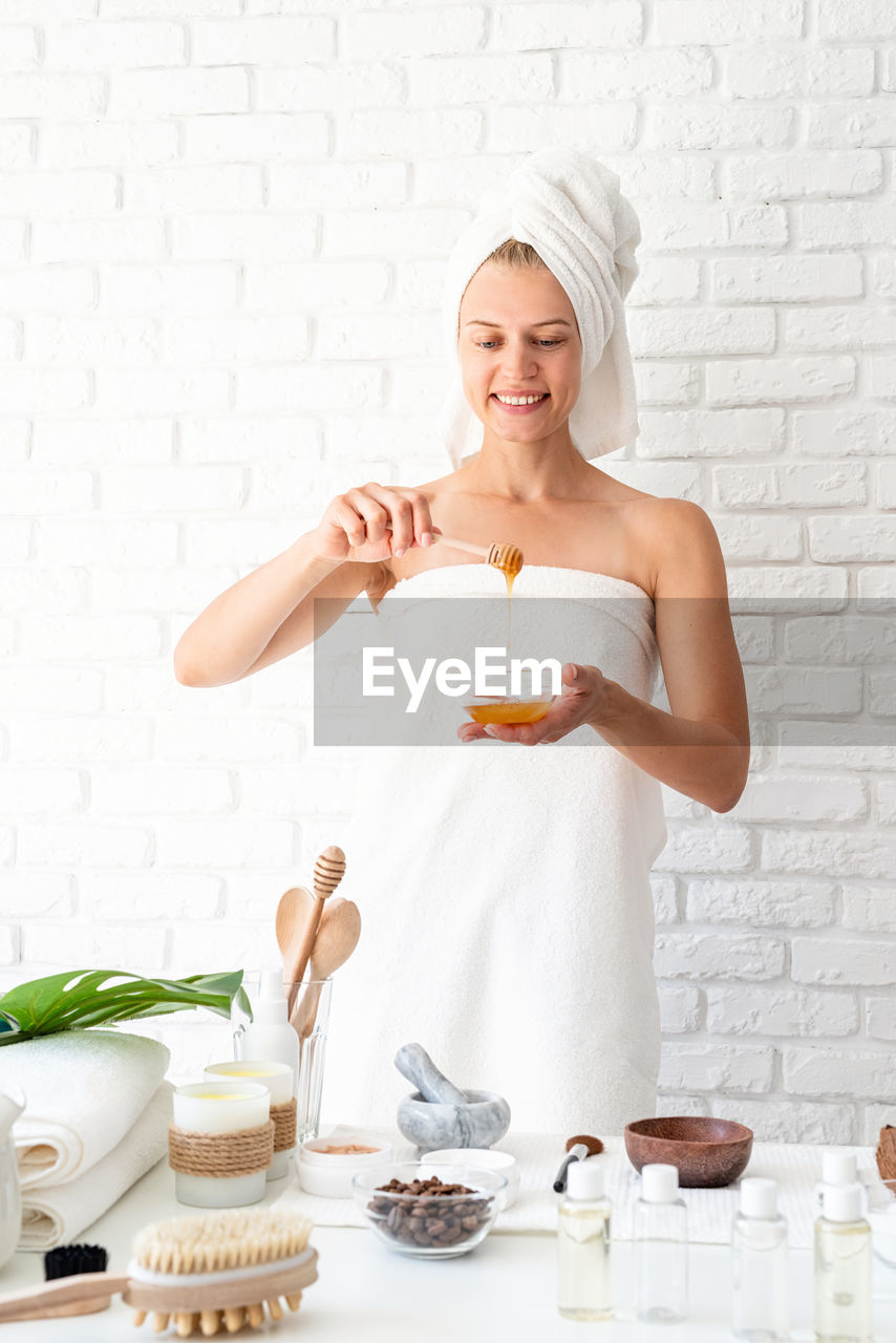 Young woman wearing white bathrobes towels on head doing spa procedures mixing natural ingredients 