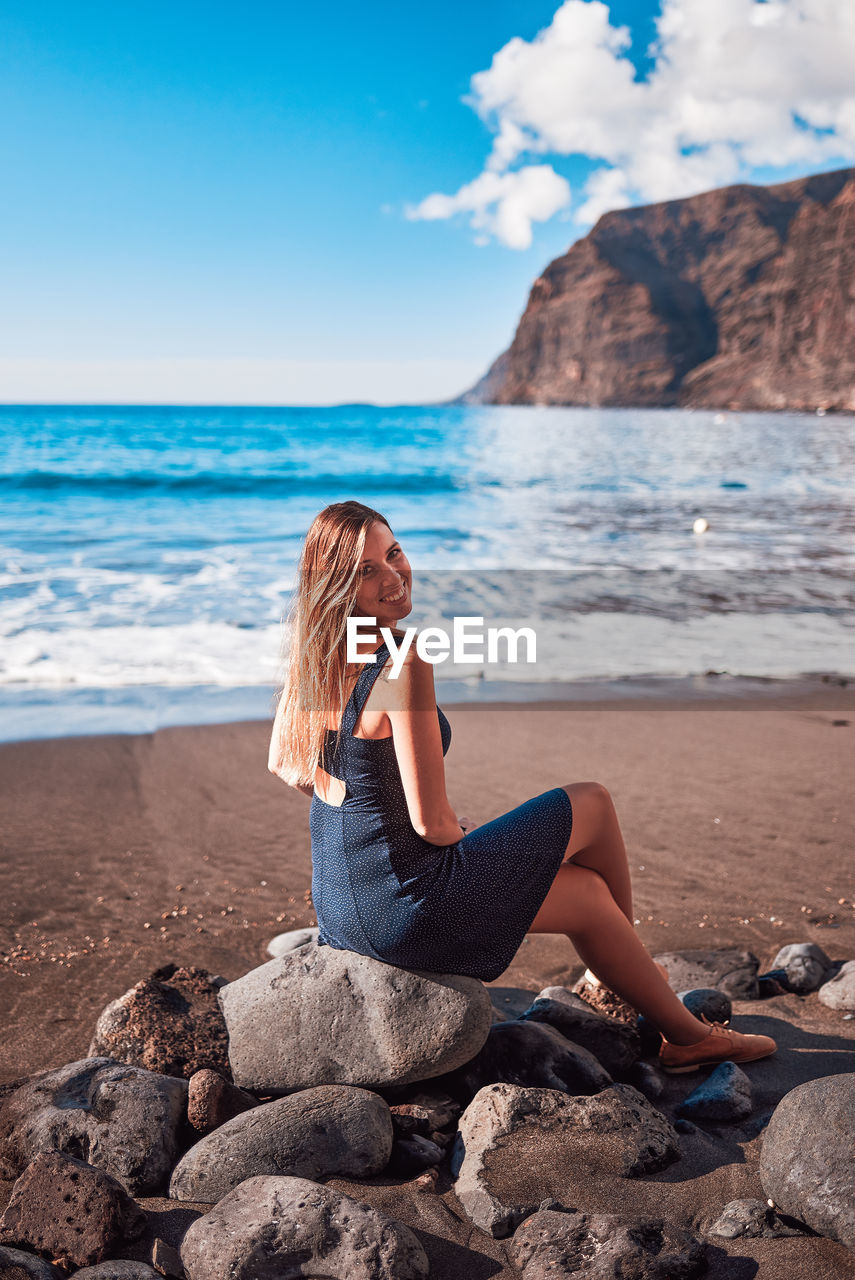 WOMAN SITTING ON ROCK AT BEACH