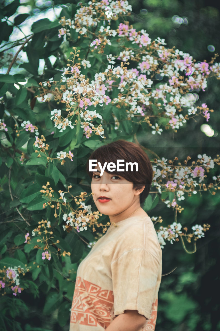 Portrait of woman standing by flowering plants