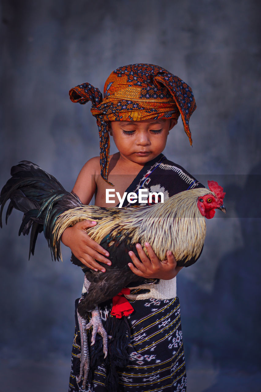 A little boy holding a rooster wearing indonesian traditional clothes 