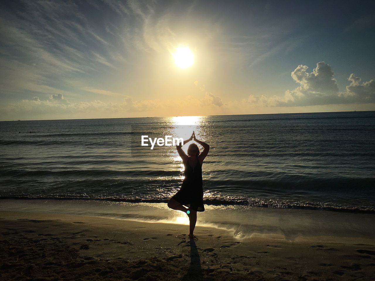 Silhouette woman exercising on beach at sunset