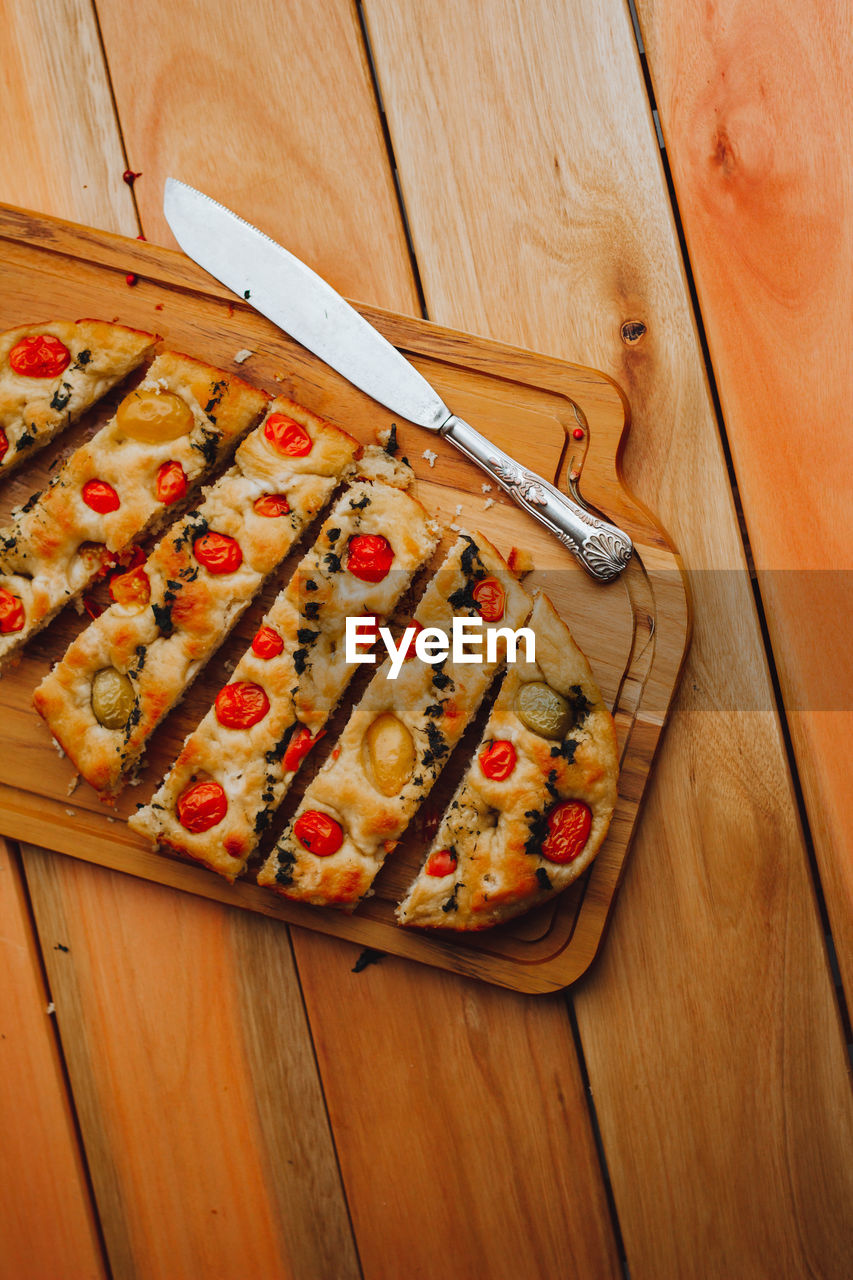 Homemade italian focaccia cut into slices, with tomato and olive oil on a rustic wooden background.