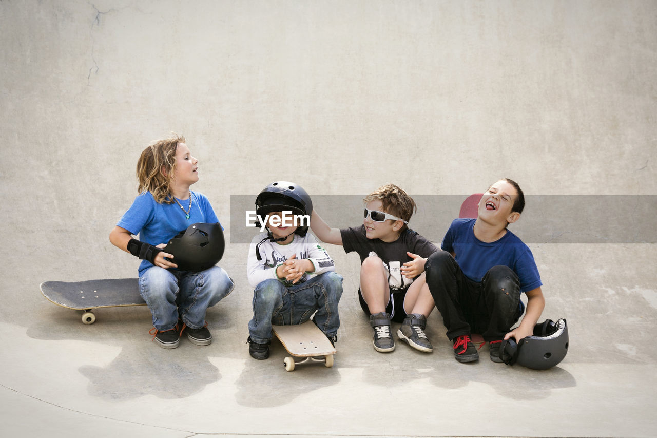 Cheerful boys talking while sitting on skateboard ramp