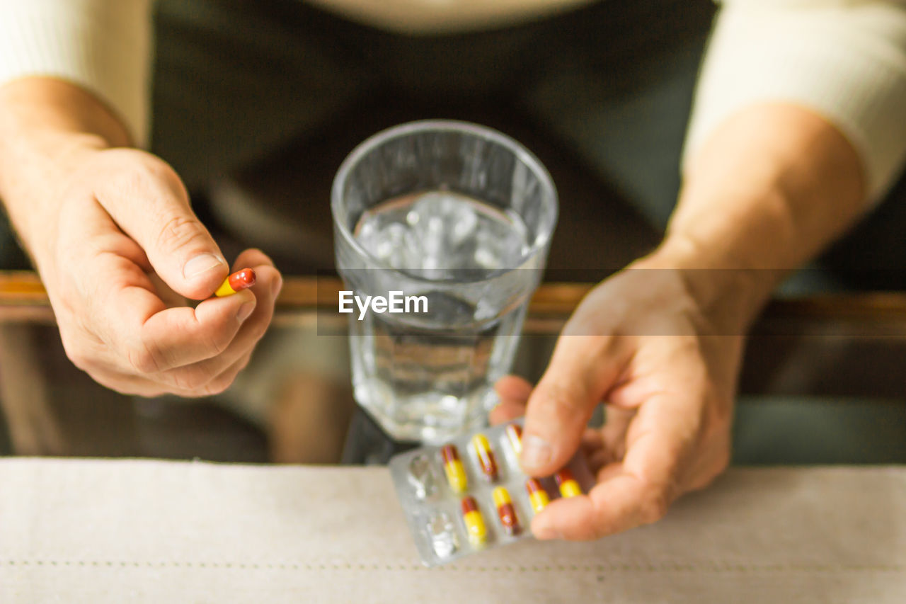 Senior man hand holds red and yellow capsule, blister of pills. ready to take medicines. health care