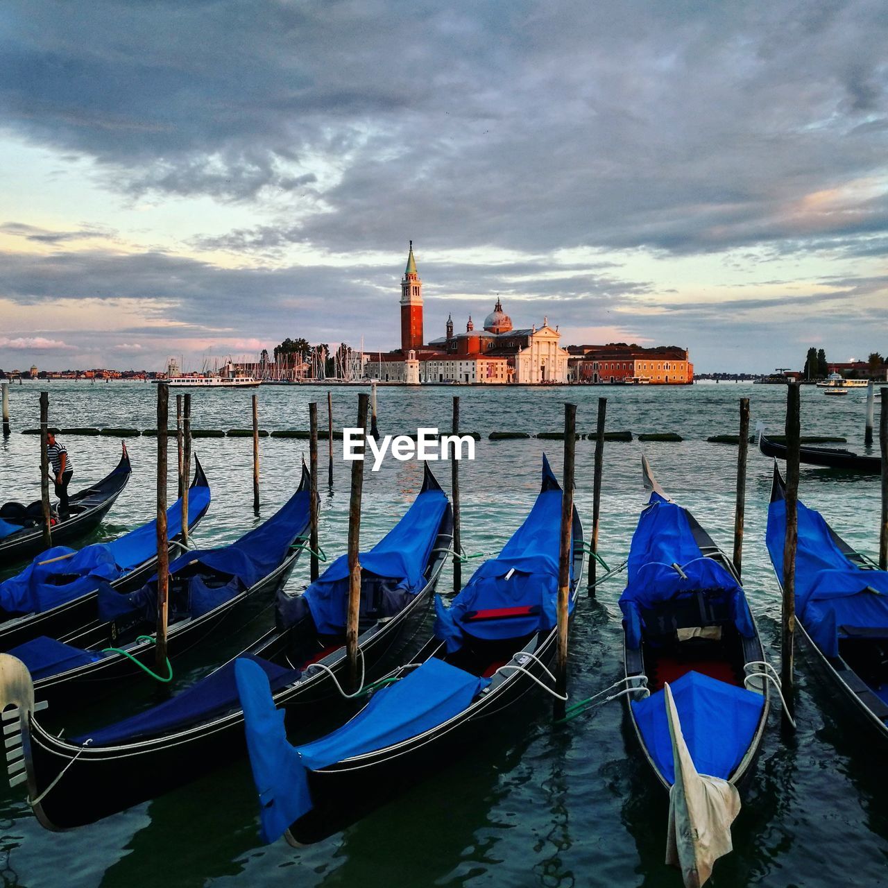 Gondola boats moored by wooden posts in grand canal against cloudy sky during sunset