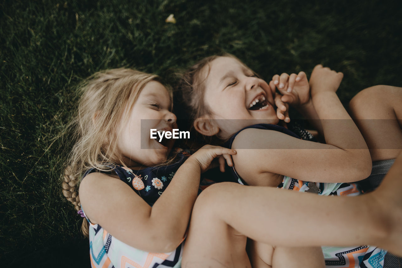 Overhead view of cheerful sisters lying on field at park