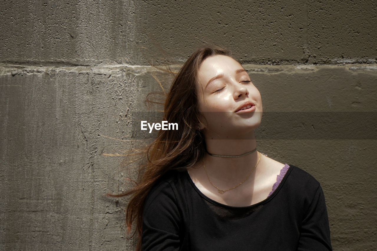 Young woman with eyes closed standing against wall