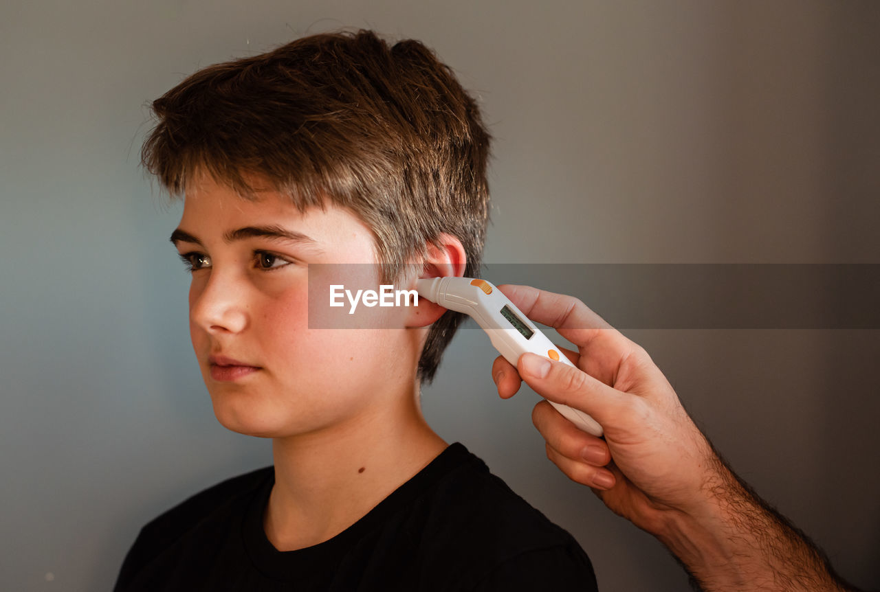 Tween boy getting temperature taken with an ear thermometer.