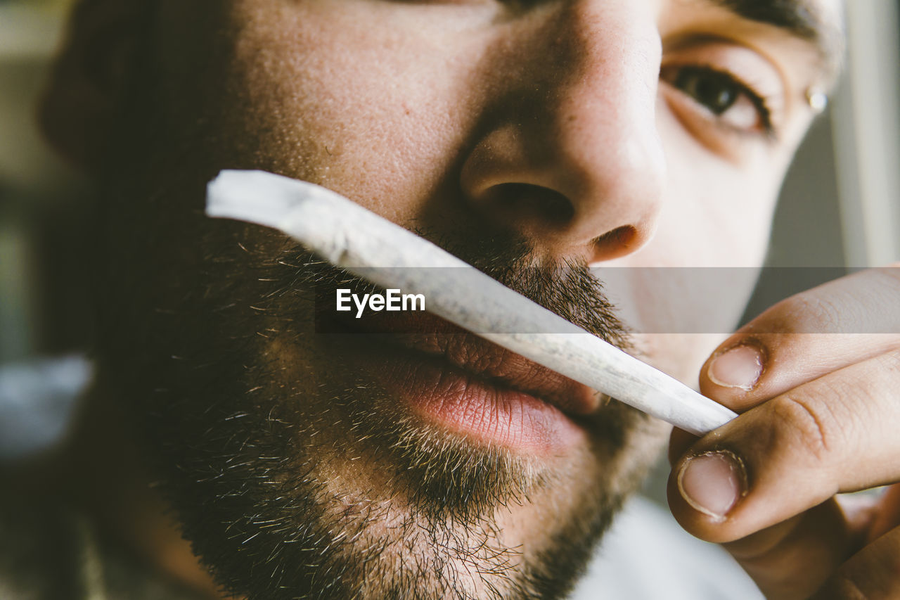 Close-up portrait of bearded man smelling marijuana joint